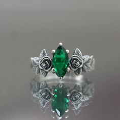 a green ring with roses and leaves on it's sides, sitting on top of a reflective surface