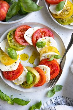 tomatoes, mozzarella and basil are arranged on two white plates with silverware