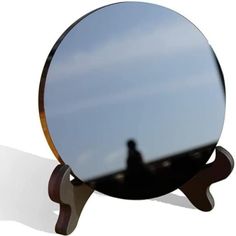 the reflection of a person standing in front of a round mirror on a wooden stand