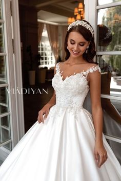 a woman in a white wedding dress standing by a window with her hand on her hip