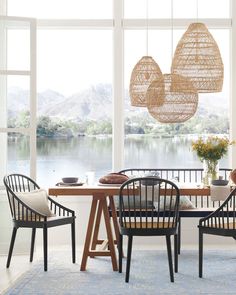 a dining room table with chairs and two hanging lights above it, in front of a lake