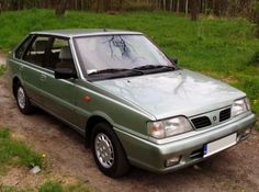 a green car parked on the side of a dirt road next to grass and trees