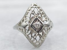 This ring has all the details of lacy Art Deco filigree: intricate crisscrossing of swirling lines, and contrasting geometric designs. Constructed of 10-karat white gold, the center of this ring features a lovely antique old mine-cut diamond, in beautiful hexagon-shaped mounting which makes the diamond appear larger. Classic Art Deco elegance!Metal: 10K White GoldGem: Old Mine Cut Diamond .09 Carats, SI1 in Clarity, I in ColorGem Measurements: 2.5 mm, RoundRing Size: 5.50Marks: "10K" Stamped on the inside band Dinner Ring, Art Deco Filigree, Estate Ring, Old Mine Cut Diamond, Estate Rings, Diamond Anniversary, Colored Gems, Round Rings, Filigree Ring