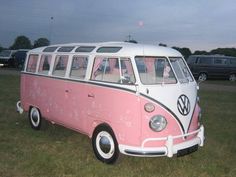 a pink and white vw bus parked in the grass