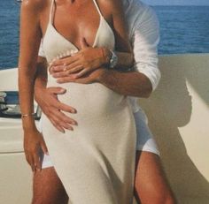 a man and woman are hugging on a boat in the ocean while one is wearing a white swimsuit