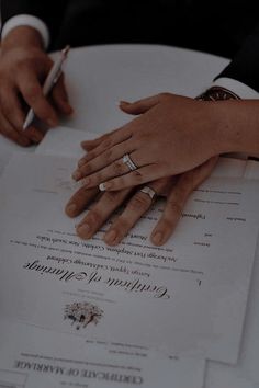 two people sitting at a table with wedding rings on their hands and papers in front of them