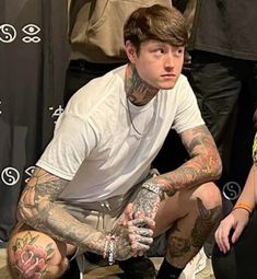 a man with tattoos sitting on the ground in front of a group of other people