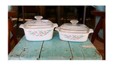 two white casserole dishes sitting on top of a blue wooden table next to each other