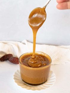 a spoon full of caramel sauce being poured into a small bowl