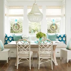 a dining room table with white chairs and blue pillows on the bench next to it