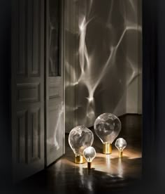 three glass orbs sitting on top of a wooden table next to a doorway with light coming through it