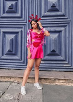 a woman standing in front of a blue door wearing a pink dress and white tennis shoes