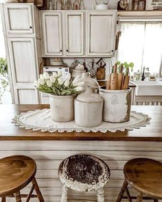 an old fashioned kitchen with white cabinets and wooden stools