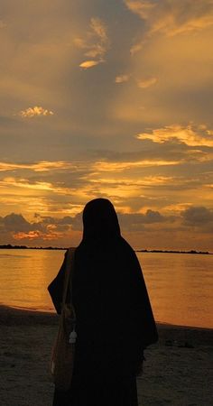 a woman standing on top of a sandy beach next to the ocean at sunset or dawn