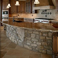 a kitchen with an island made out of stone and wooden cabinets, lights hanging from the ceiling