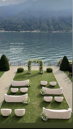 an outdoor wedding setup with white couches and greenery on the lawn by the water