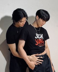 two young men standing next to each other in front of a wall with their hands on their hips