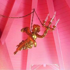 a gold angel statue hanging from a pink ceiling