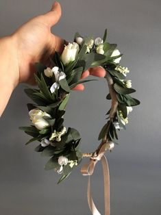 a hand holding a wreath with white flowers and greenery