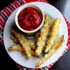 a white plate topped with fried zucchini fries next to a bowl of ketchup