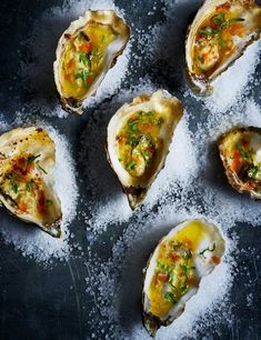 six oysters with various toppings on a black plate covered in salt and pepper