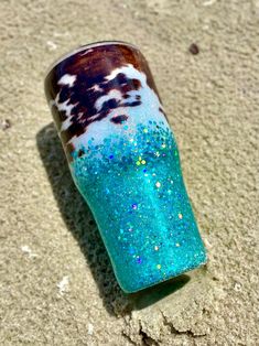 a blue and brown cup sitting on top of sand