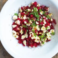 a white bowl filled with chopped vegetables on top of a wooden table next to a fork