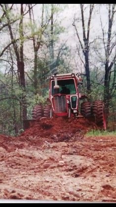 a red tractor is parked on top of a pile of dirt in front of some trees