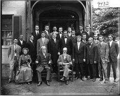 a group of men in suits and ties posing for a photo outside an old building