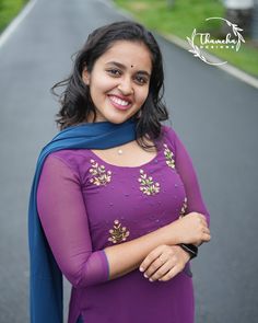 a woman standing on the side of a road wearing a purple dress and blue shawl