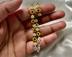 a hand holding a beaded bracelet with yellow and white flowers on it's sides