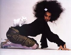 a woman with an afro holding a white cat in her lap and sitting on the floor