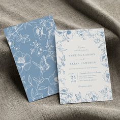 two blue and white wedding cards sitting on top of a bed next to each other