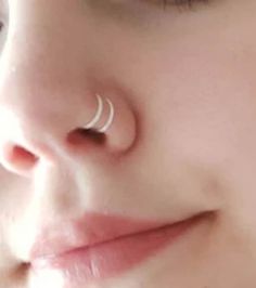 a woman's nose with a single white ring on her nose and an ear piercing