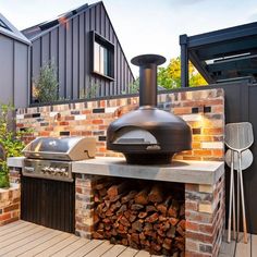 an outdoor bbq grill with wood stacked on the outside and brick walls surrounding it