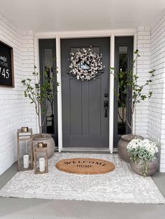 a welcome mat on the front door of a house with potted plants and lanterns