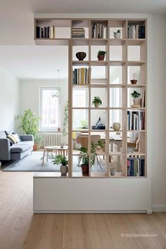 a living room filled with furniture and bookshelves next to a window covered in plants