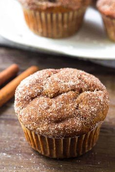 cinnamon sugar muffins on a plate with cinnamon sticks next to it and another muffin in the background