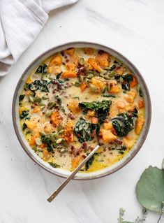 a bowl of soup with spinach, carrots and other vegetables on a white table