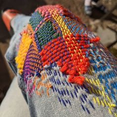 someone is sitting on a bench with their hand knitted sweater over his leg and the colors of the fabric are multicolored