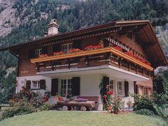 a house with flowers on the balconies in front of it and mountains in the background