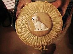 a small white dog sitting on top of a straw bag with an oval frame around it