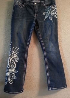 a pair of blue jeans with white flowers on them hanging from a hook against a wall