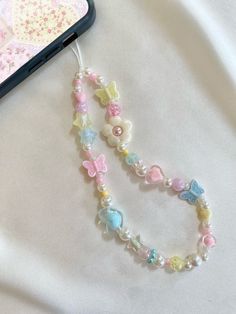 a cell phone is laying next to a beaded necklace on a white sheet with pink, blue and yellow flowers