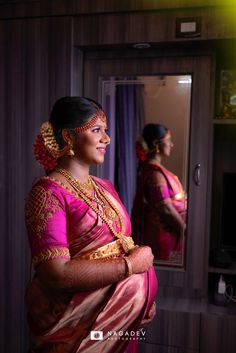 a woman standing in front of a mirror wearing a pink sari and gold jewelry