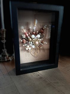 a framed photograph with beads and other items in it on a table next to a candle