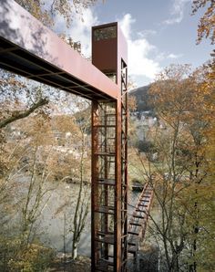 a tall metal structure sitting on top of a lush green hillside next to a river