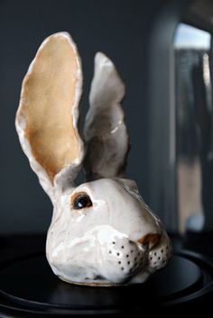 a ceramic rabbit head sitting on top of a black table next to a glass vase