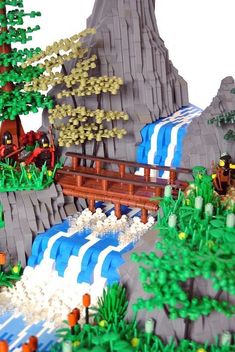 a lego model of a waterfall and bridge with trees on each side, in front of a mountain