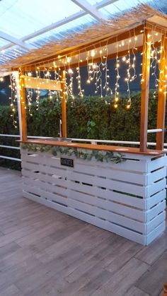 an outdoor bar made out of pallets with lights strung from the roof above it